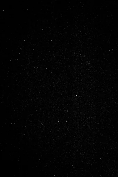Tiny white stars scatter thinly across a tall, almost lightless sky — close to true black through most of the frame.