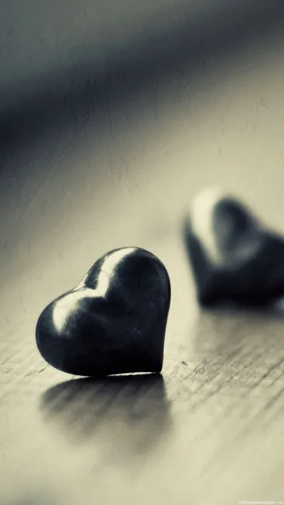 A polished black heart sits on a wooden surface in a tall crop, a second one out of focus behind it in muted grey-blue light.