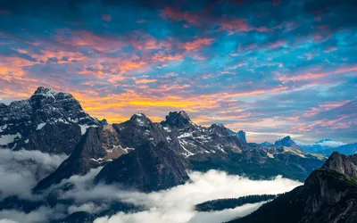 Orange and blue clouds sweep above serrated peaks while a sea of cloud pools in the valley, the near-black foreground ridge suiting OLED screens.