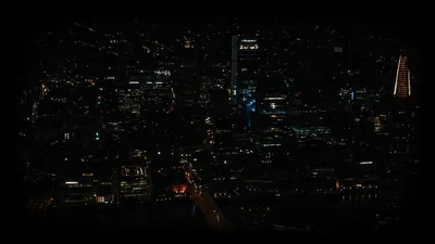 Office towers seen from above keep only a few lit floors, one red-lit avenue cutting through an otherwise unlit grid.