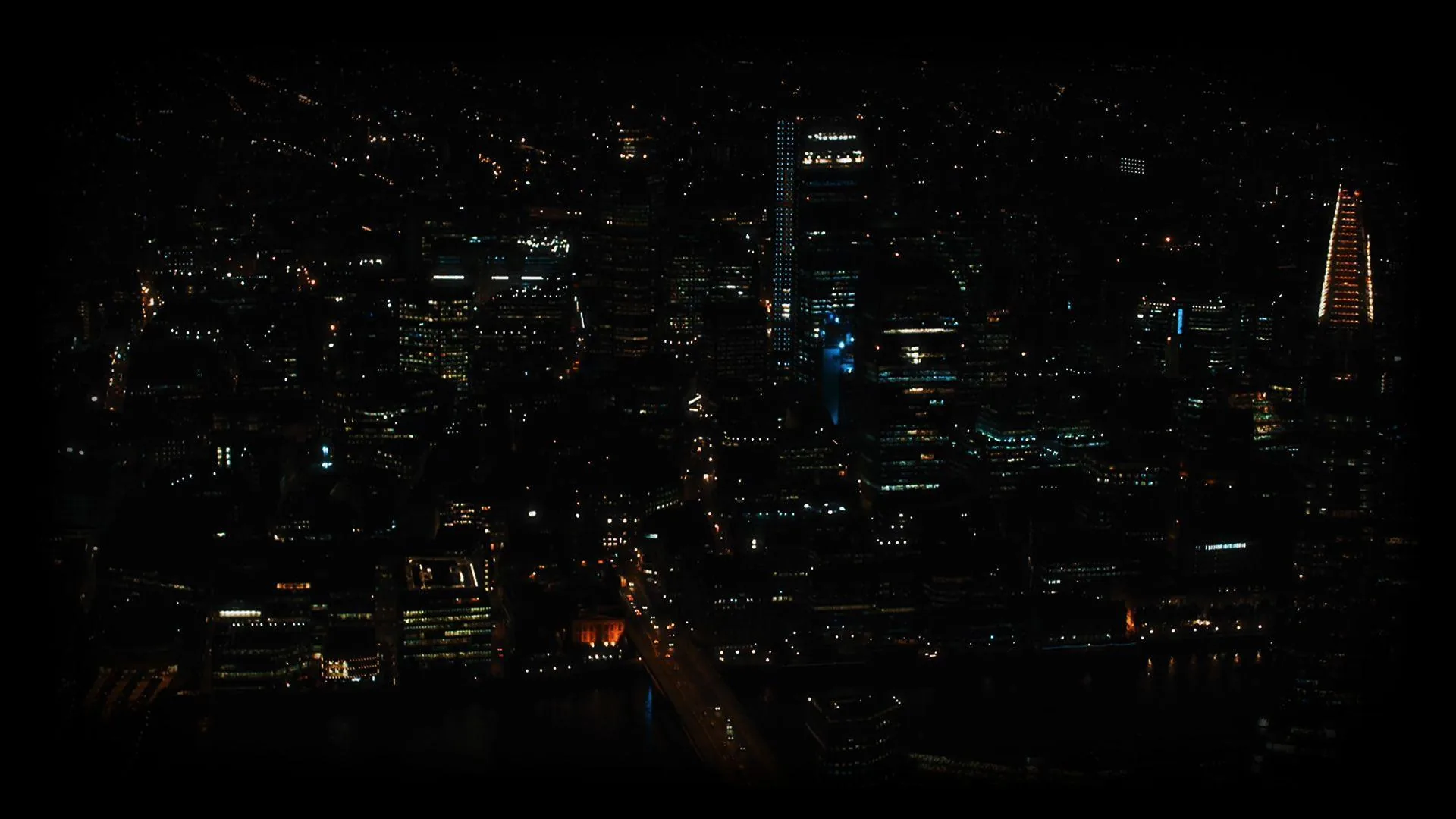 Office towers seen from above keep only a few lit floors, one red-lit avenue cutting through an otherwise unlit grid.