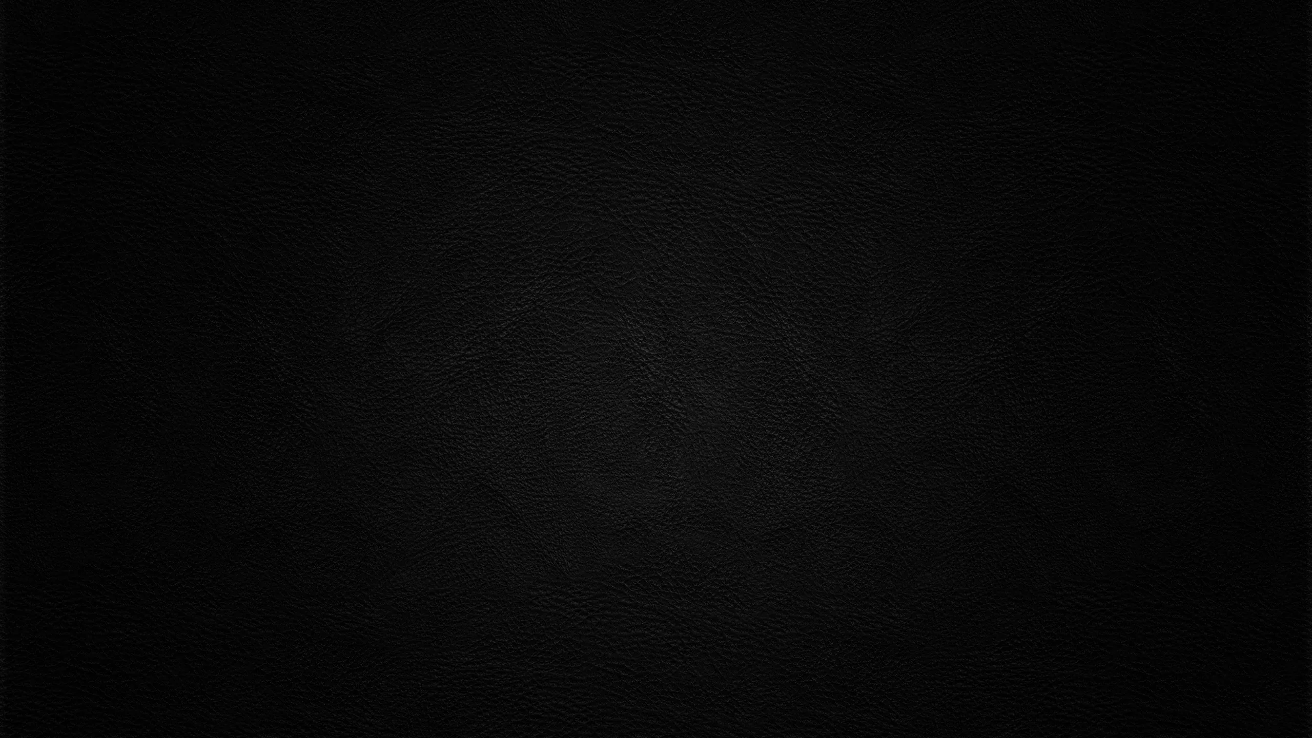 A flat dark wall with a barely-there grain, a hint of lift near the centre and full black at the edges.