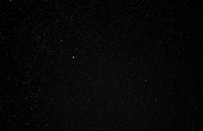 A wide-open night sky covered in fine white stars, with one brighter point sitting just above the centre.