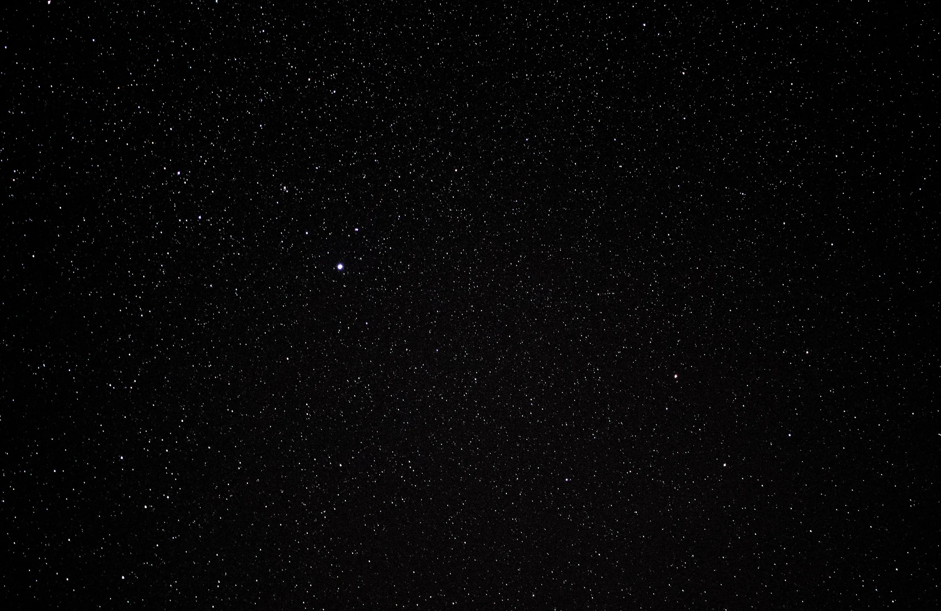 A wide-open night sky covered in fine white stars, with one brighter point sitting just above the centre.