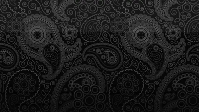 Paisley shapes and rosettes press into a dark grey surface with only their outlines catching light, a diffuse glow across the middle of the frame.