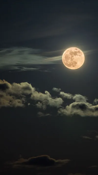 An amber-toned full moon sits in the upper half while pale clouds stack along the bottom, the mid-frame gap dark enough for lock-screen text.