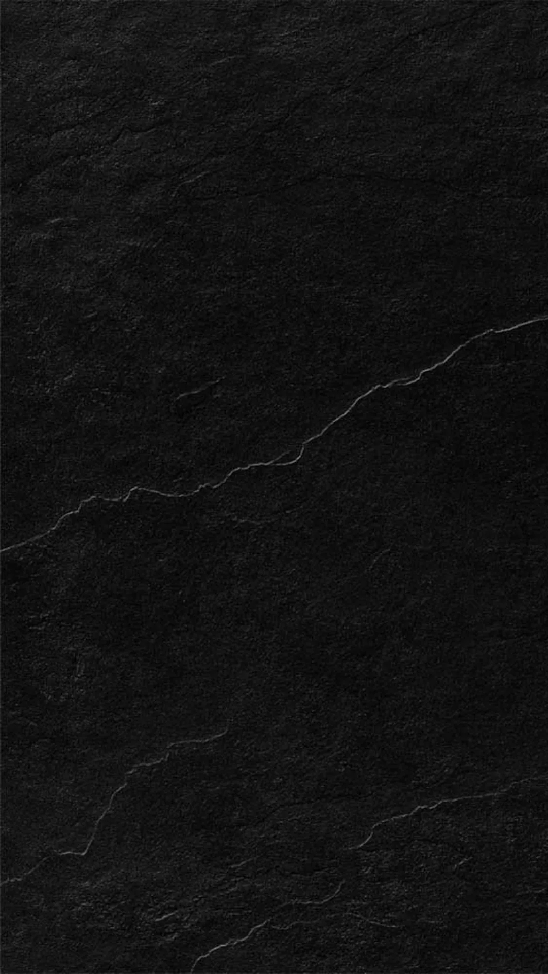 Rough slate fills the frame in deep black, thin pale cracks branching from the right edge across the middle while the base stays clean.