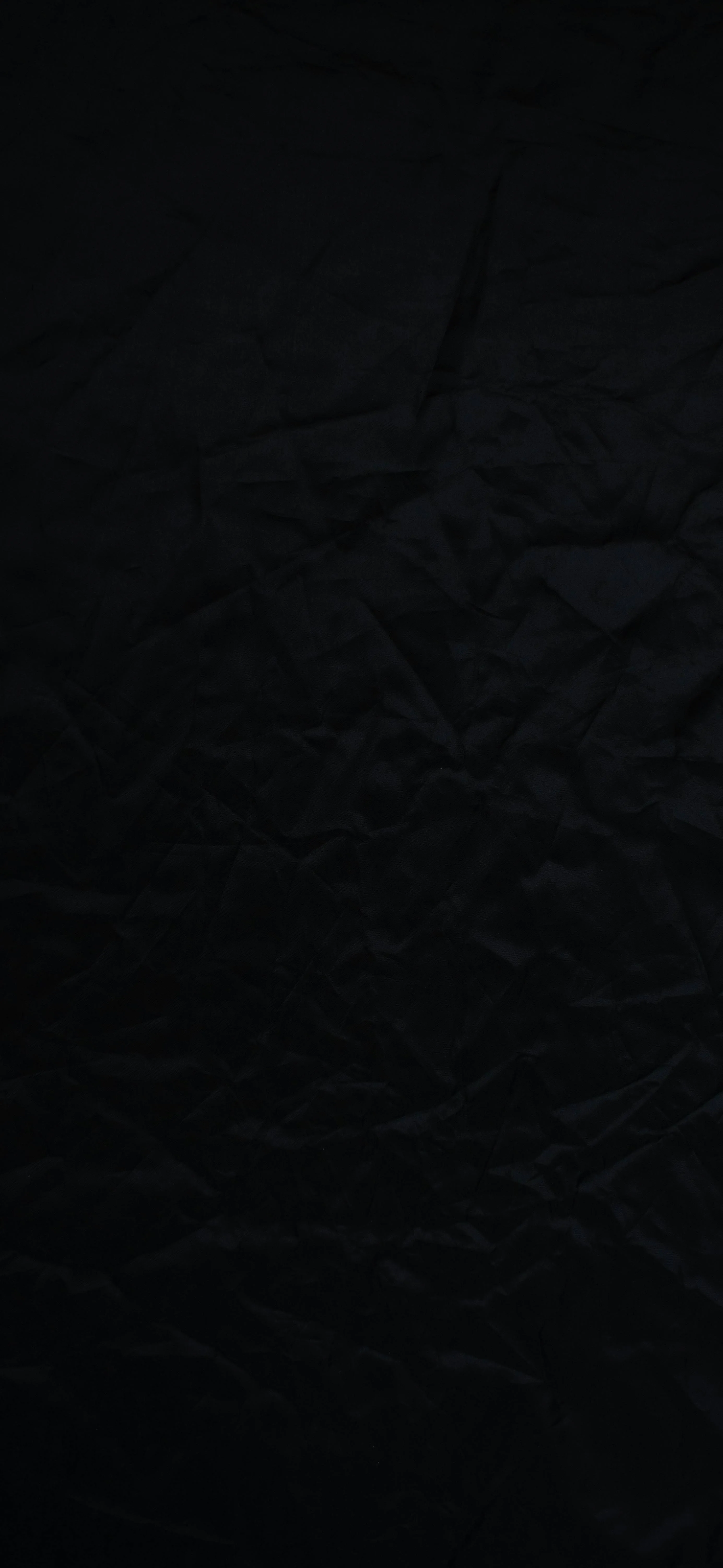 A sheet of black paper covers the tall frame edge to edge, its creases only visible where a weak light rakes across the upper half.