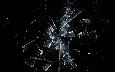 Broken glass bursts outward mid-air on a pure black field, each shard edged in white with a spray of fine splinters around it.