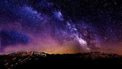The galactic band curves over dark peaks, violet overhead fading to amber at the horizon — the top corners stay dark for status bar text.