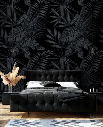 Tropical palm and fern leaves printed black on black fill the wall behind a tufted bed, readable only where the light grazes them.