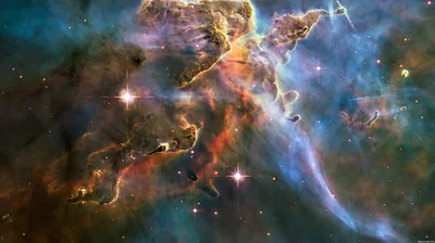 Hubble's view of dust pillars in the Carina Nebula, amber peaks climbing through blue-green gas with newborn stars firing jets from their tips.