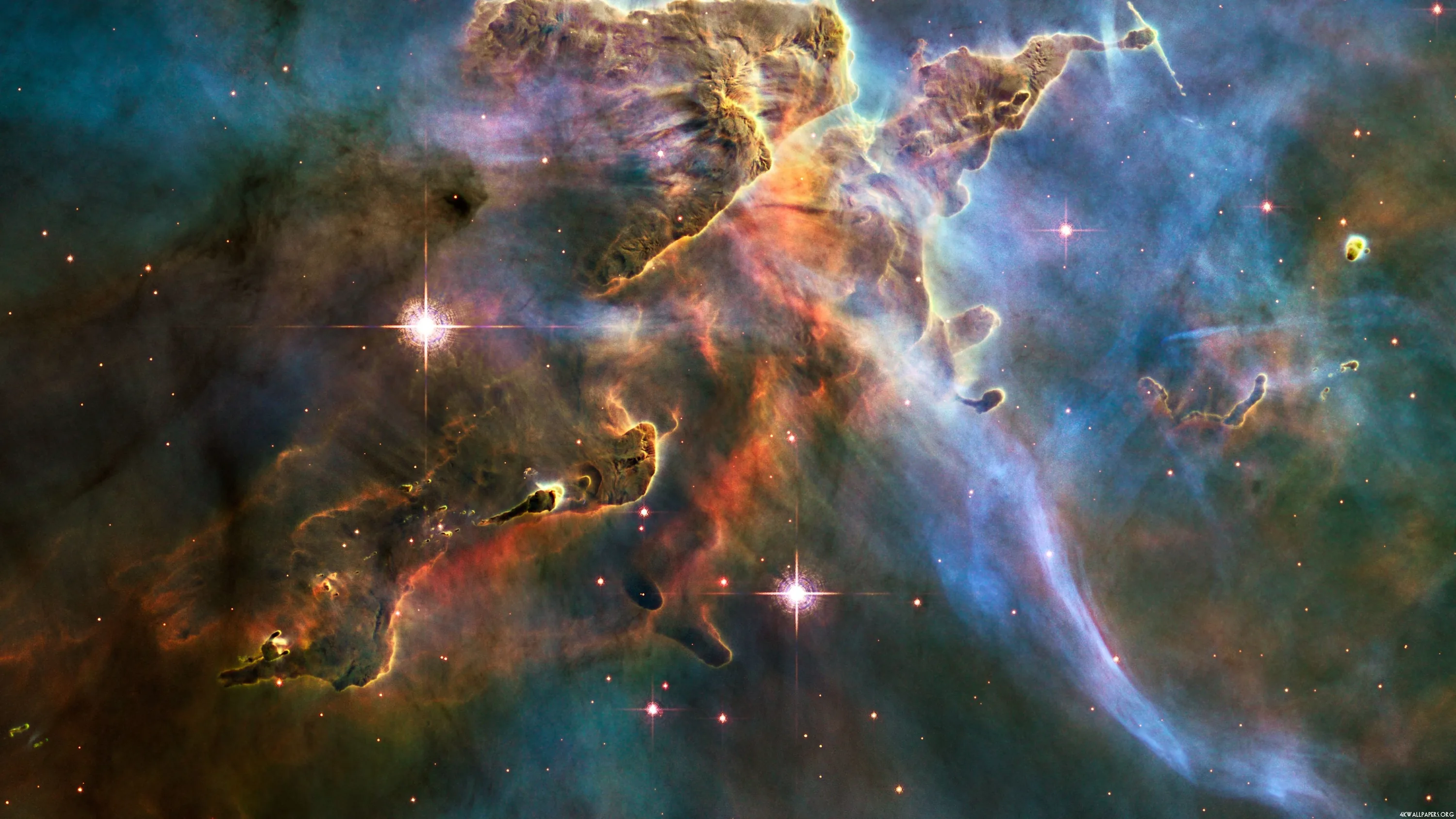 Hubble's view of dust pillars in the Carina Nebula, amber peaks climbing through blue-green gas with newborn stars firing jets from their tips.