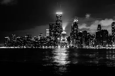Downtown lights burn against a black sky and black water, with the tallest tower catching a soft halo of low cloud.