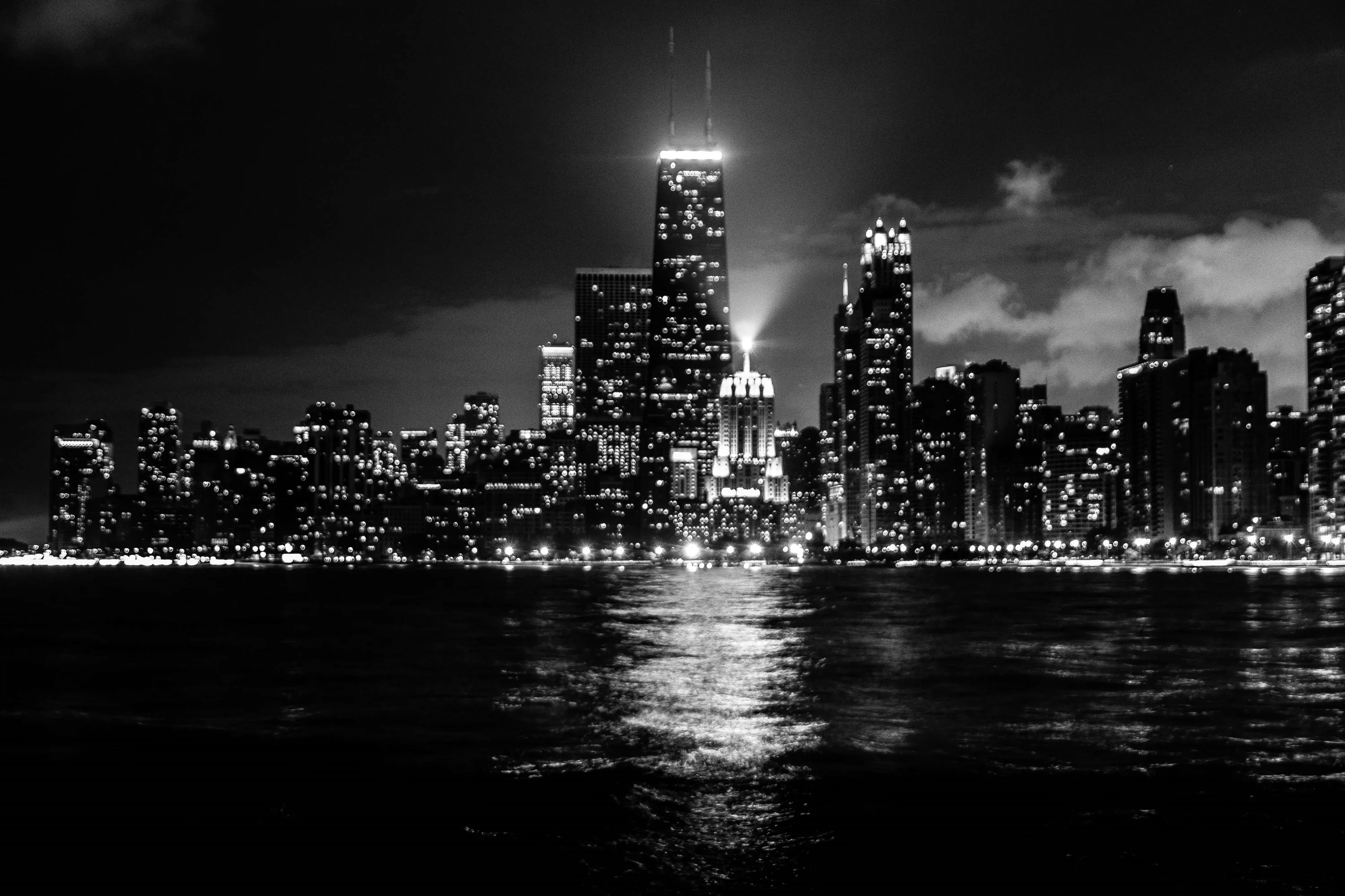 Downtown lights burn against a black sky and black water, with the tallest tower catching a soft halo of low cloud.
