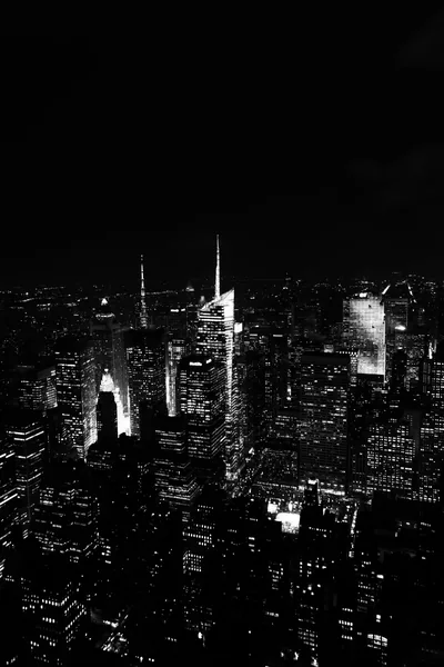 Towers crowd the lower half of the frame in hard monochrome, one antenna spire catching light while the streets stay black.
