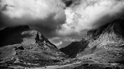 Two rocky peaks frame a scree-filled pass as heavy cloud rolls over the ridge, contrast pushed hard into the rock faces.