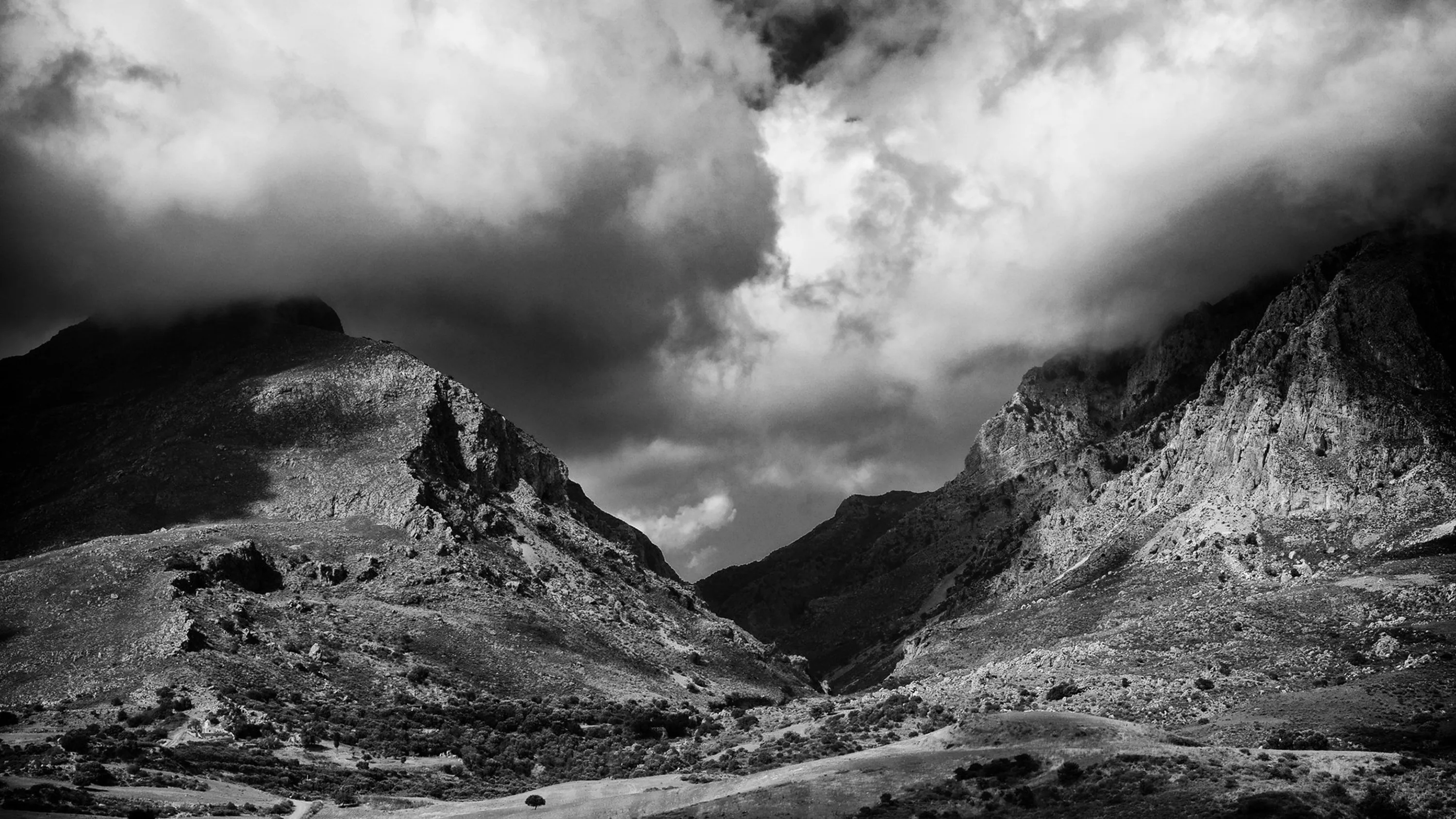 Two rocky peaks frame a scree-filled pass as heavy cloud rolls over the ridge, contrast pushed hard into the rock faces.