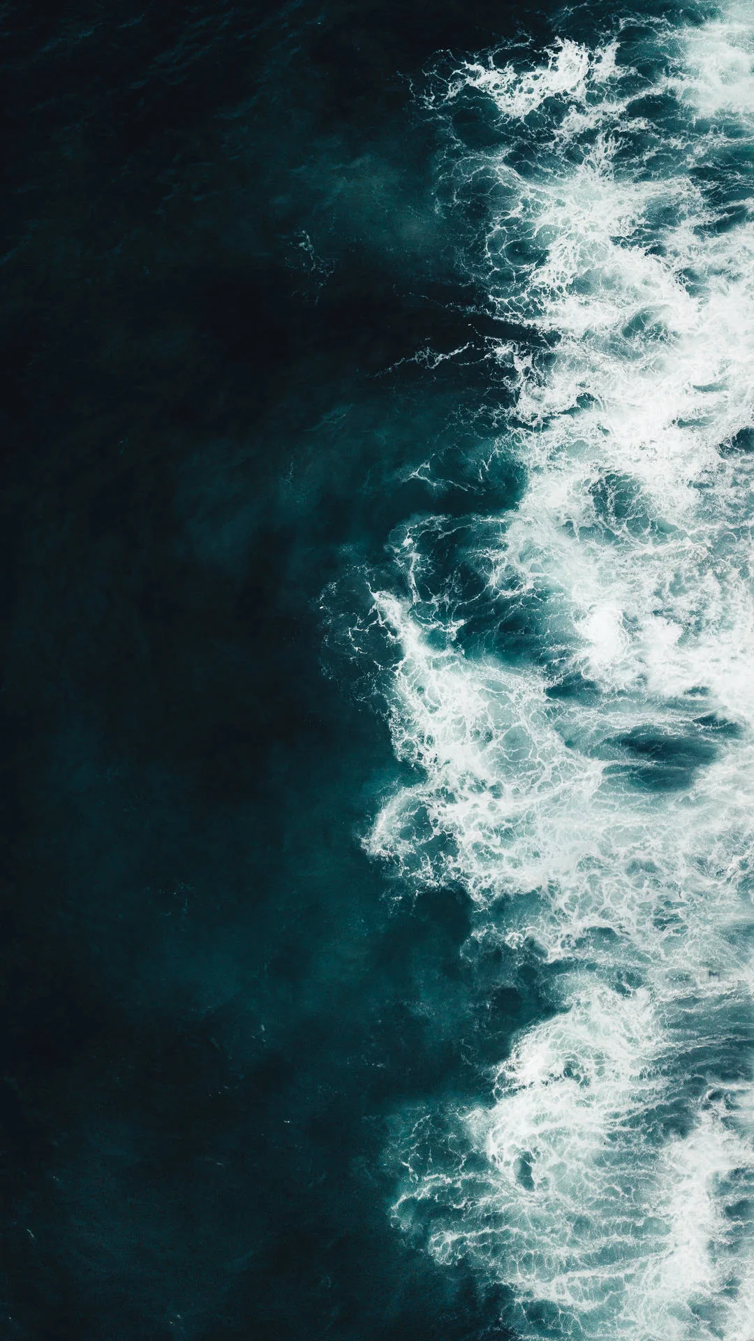 Shot straight down, white surf churns along the right side of the frame while the left half stays calm teal, clear space for a clock.