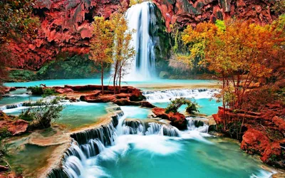 Twin plumes drop from a red rock ledge into stepped blue-green terraces, autumn trees flanking the falls; the churning foreground leaves no quiet space for widgets.