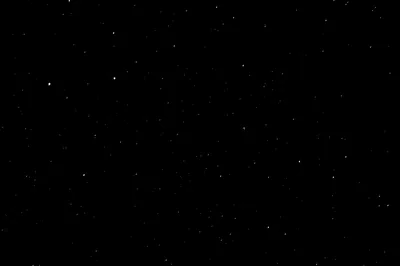 A scattering of small white stars across an almost unbroken night sky, no moon and no horizon, the frame reading as true black on OLED.