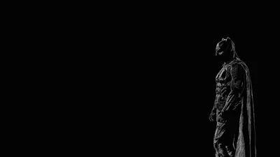The cowled figure stands at the right edge in near-black monochrome, cape hanging straight down, the whole left two-thirds of the frame left empty.