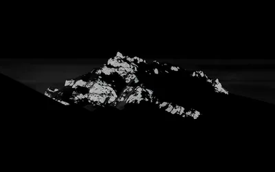 One rock summit catches hard light while the slopes and sky around it drop away into black, monochrome and nearly silhouetted.
