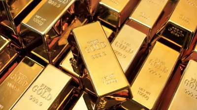 Minted 999.9 fine gold bars stacked in loose rows, one bar angled across the pile with its stamped face in sharp focus.