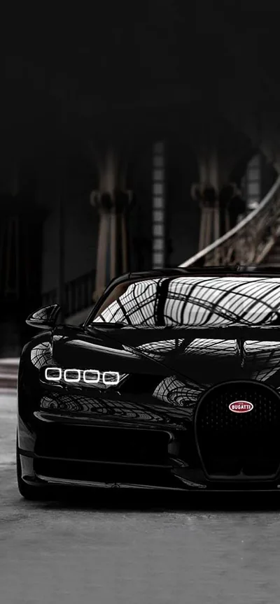 Vertical framing of a Chiron parked inside a wide hall, the arched ceiling reflected across its bonnet and the badge on the nose the only spot of colour.