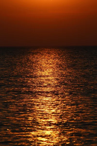 Nothing but water: low sun glitter scattered across small ripples under a deep amber sky, the horizon reduced to a thin black band.