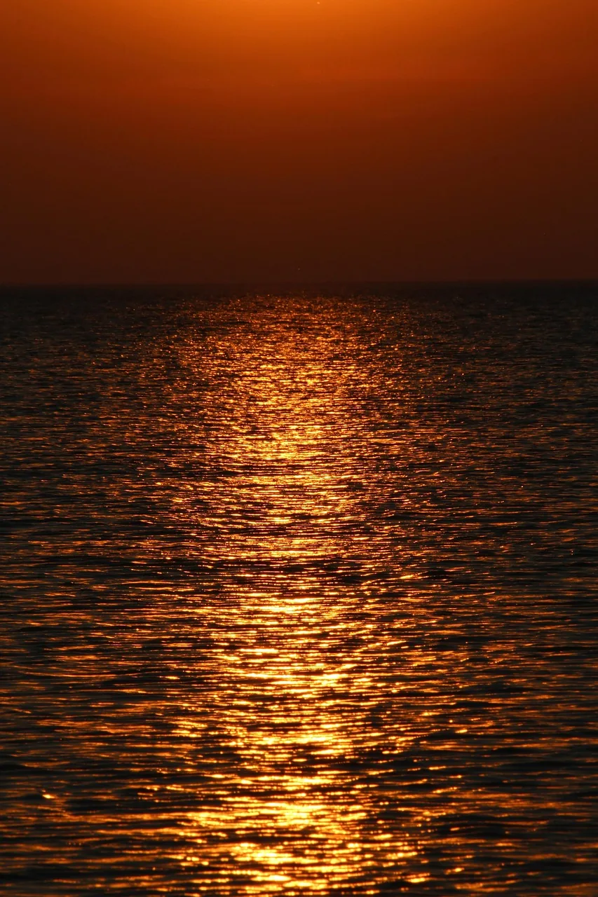 Nothing but water: low sun glitter scattered across small ripples under a deep amber sky, the horizon reduced to a thin black band.