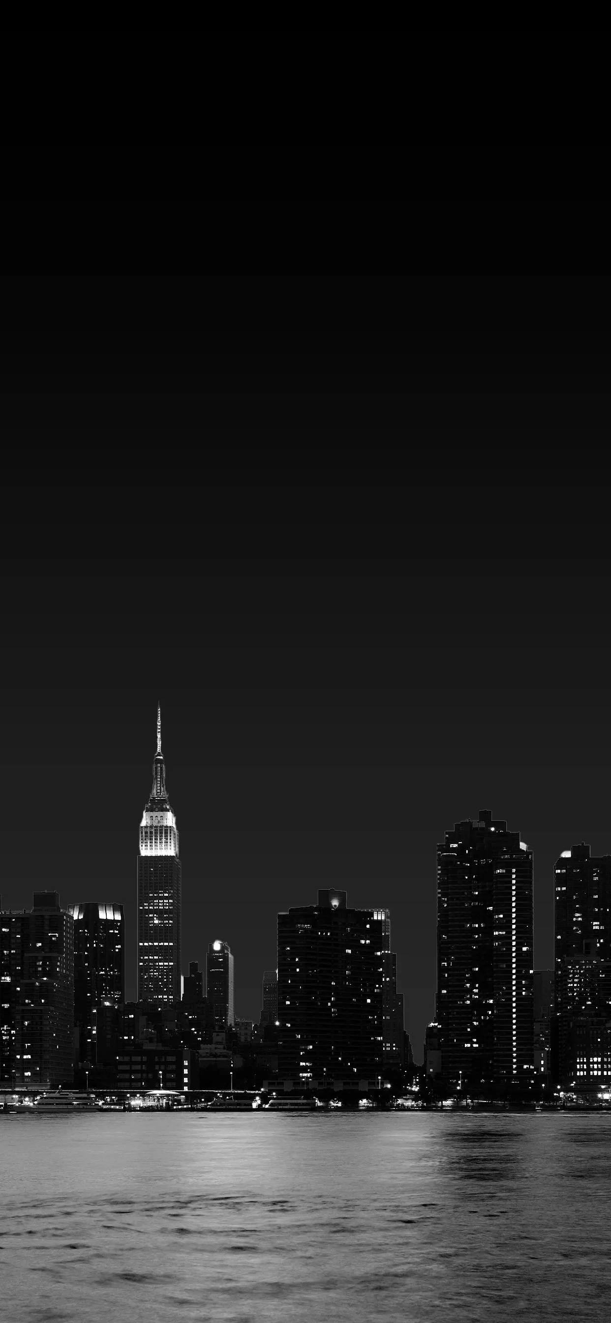 A river of dark water in the foreground, tower lights scattered across the skyline behind, one tall spire lit brightest at the centre.