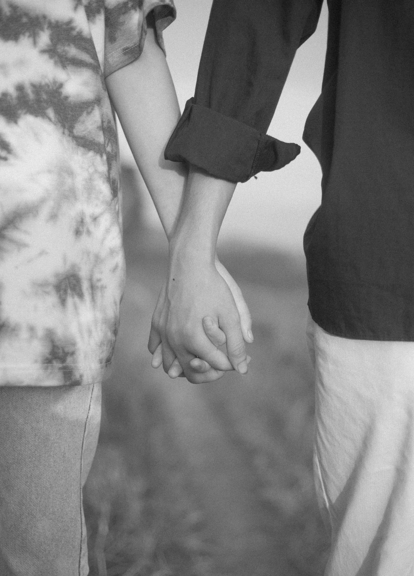 Two people walk side by side with fingers laced, cropped at the waist so the joined hands sit centre frame in soft monochrome.