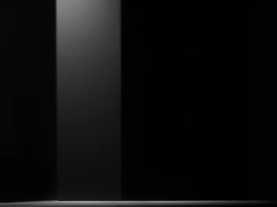 One pale grey column of light stands against a black studio wall, its reflection stopping short on the floor below.