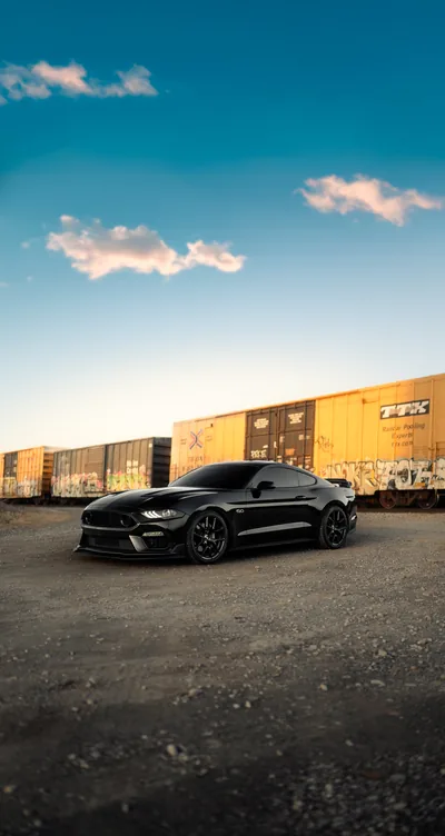 A lowered Mustang parked against a wall of yellow shipping containers, deep blue sky and thin clouds filling the top half of the frame.