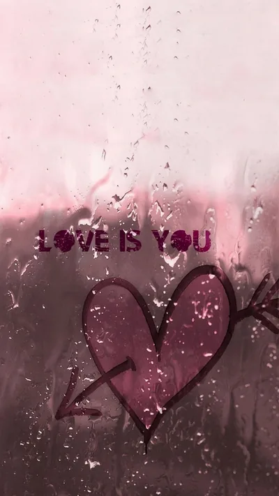 A finger-drawn heart pierced by an arrow and the words love is you sit on fogged glass, rain running down the pink pane.