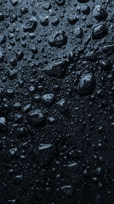 Beads of water sit across a slab of wet black stone, the largest drops clustered in the upper half and each holding its own highlight.
