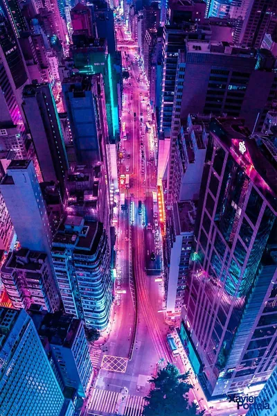 Looking straight down into a canyon of tower blocks, a pink-lit road threads the centre — the buildings on both sides fall dark enough to hold app icons.