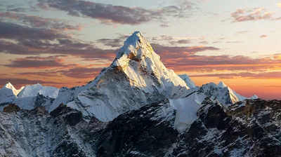 A pyramid-shaped snow peak catches the last gold light beneath streaks of orange cloud, the dark rocky base anchoring the frame.