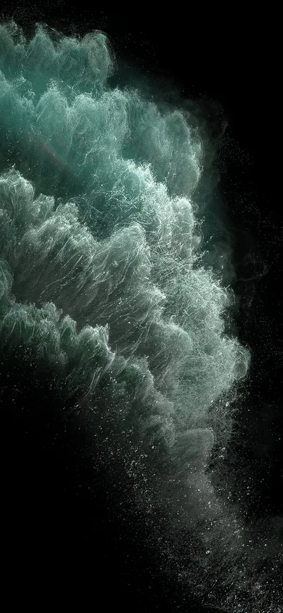A wave breaks in a spray of teal and white foam against black water, the crest lit from one side and the lower frame left almost empty.