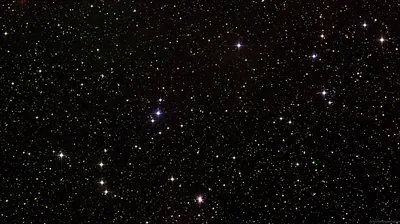 Thousands of stars scattered across black sky, a few burning blue and orange, the rest fading to faint dust.