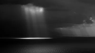 Sunbeams break through storm clouds onto a bright patch of sea at the left, the rest of this black and white seascape staying dark enough for icons.