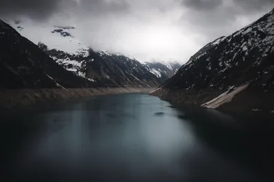 Still grey water runs between snow-streaked slopes with low cloud sitting on the peaks at the far end.