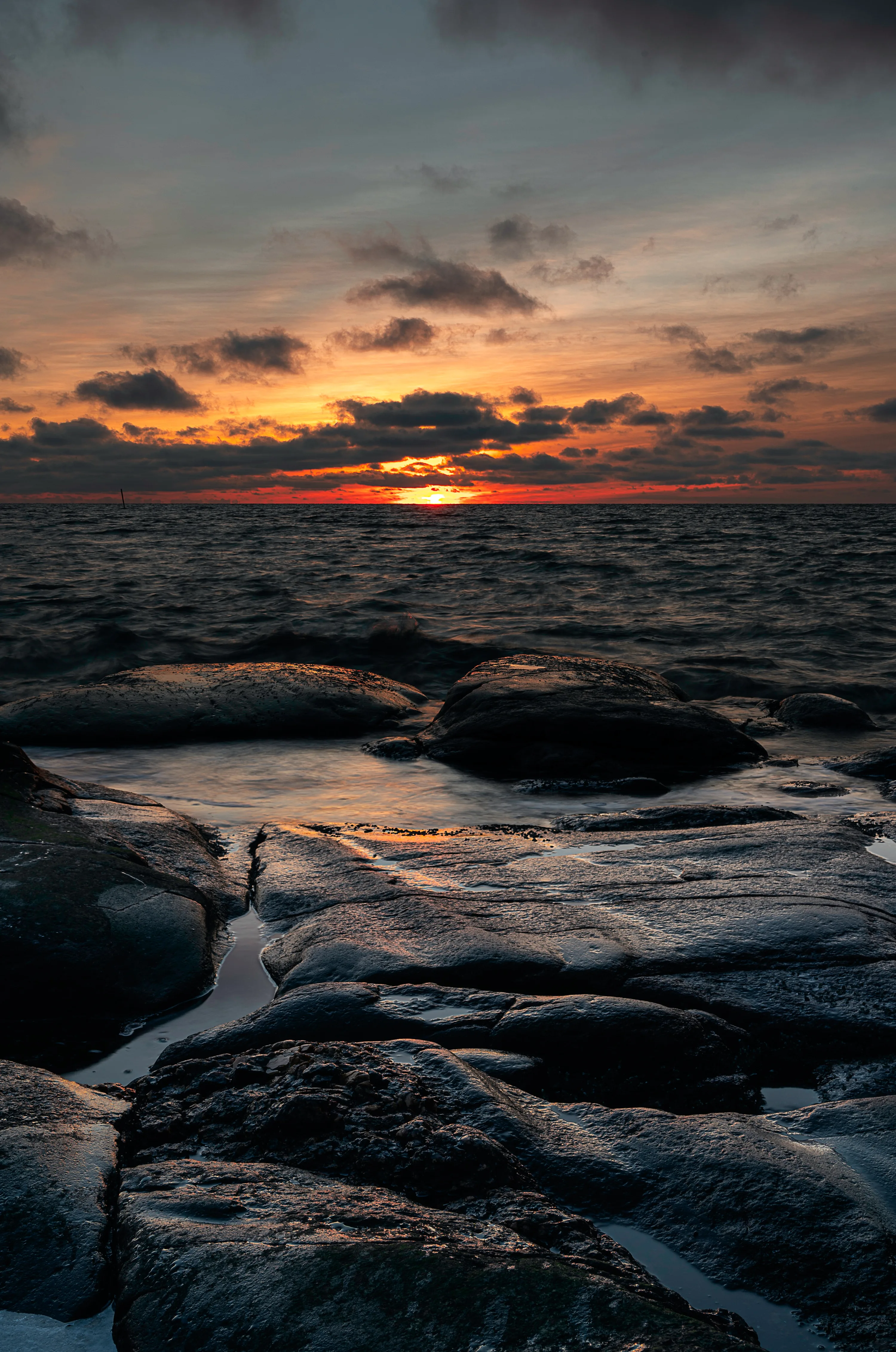 Cracked slabs of wet rock catch the last orange light at the horizon, the sky above left dark enough for a lock-screen clock.