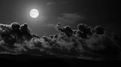 Moonlight rakes across a row of heavy storm clouds from the upper left in stark black and white, the ridge below sunk in darkness.