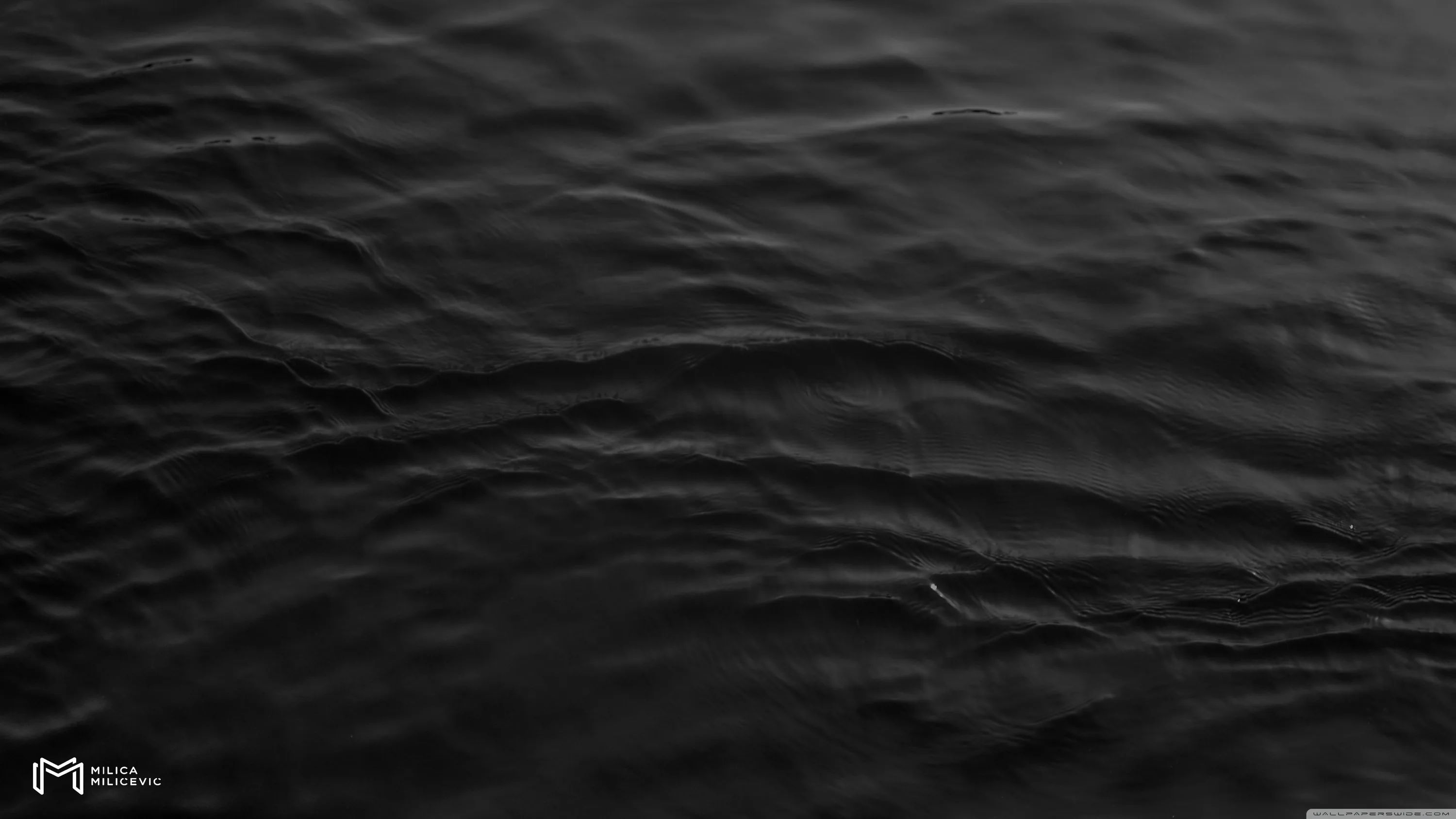 Low ripples cross the surface of black water, the light skimming their crests in grey and leaving the troughs almost invisible.