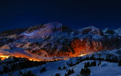 Warm town lights set the base of a snowy massif glowing orange against the blue night, the plain snowfields in front staying free of detail.