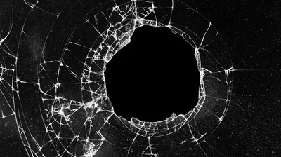 A wide black gap sits at the centre of a spiderweb of cracks, the splintered glass brightest close to the break.