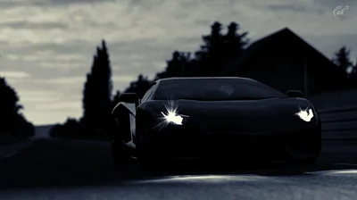 Almost the whole frame is dark blue — only the headlights, a strip of guardrail and the edge of a barn roof separate the car from the evening sky.