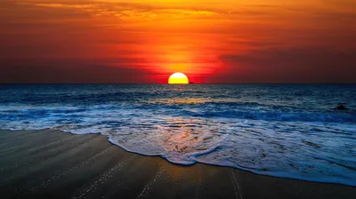 Only the top of the sun still shows above a dark red sea, a lace of white foam sliding up the sand at the bottom of the frame.